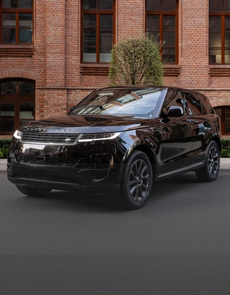 Чёрный Range Rover Sport, припаркованный на фоне кирпичного дома и зелени.