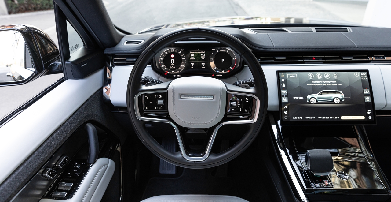 Салон Range Rover Sport с видом от водителя: цифровая панель приборов, мультимедийный экран, кожаный руль и лаконичный интерьер в серо-чёрных тонах.