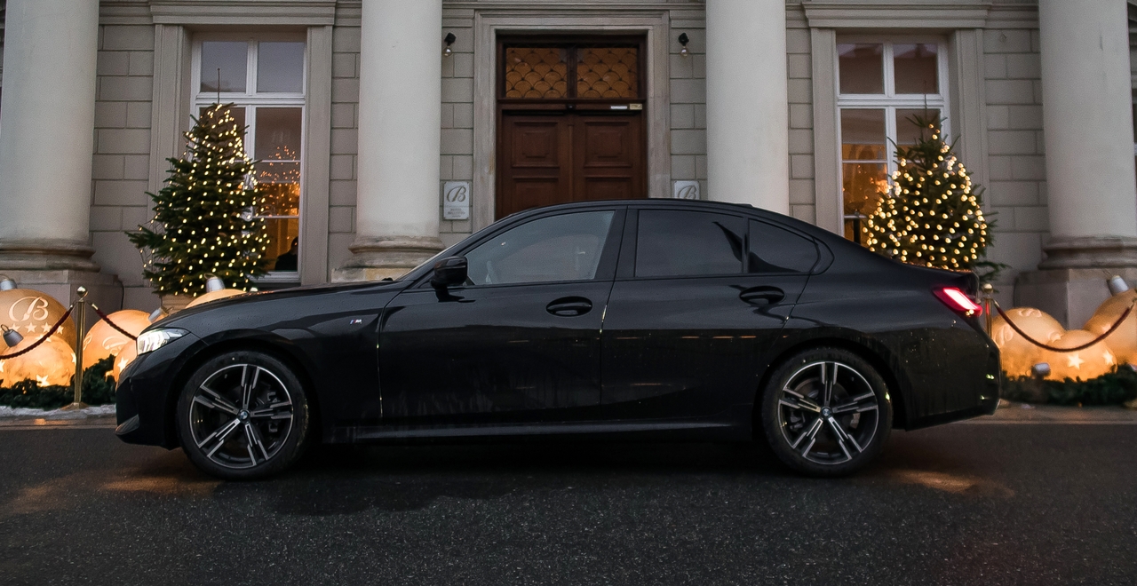 BMW 3 Series с элегантным дизайном у стильного фасада, идеально подчеркивает рождественское настроение с огнями и елками. Взять эту машину напрокат легко на сайте SK Cars.