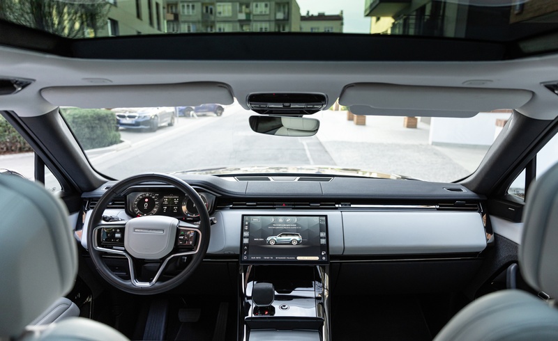 Вид из салона Range Rover с панорамной крышей, цифровой приборной панелью и большим сенсорным дисплеем по центру.