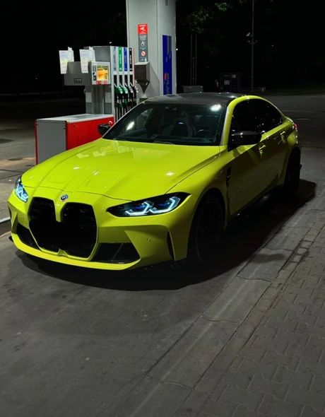 Жёлтый BMW M3 Competition с включёнными фарами на ночной заправке
