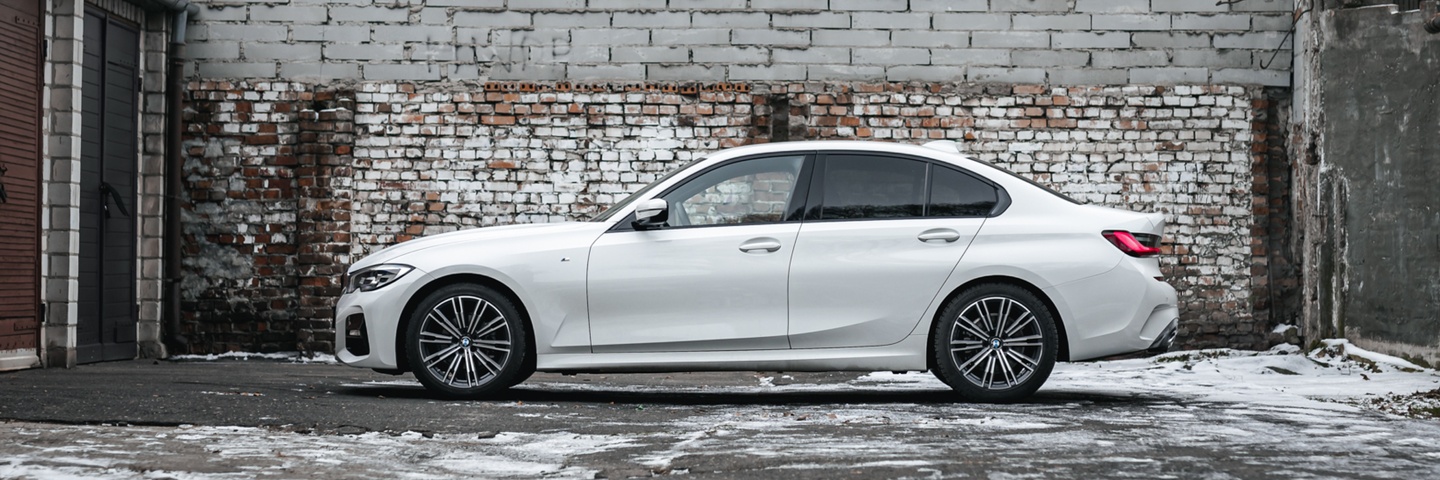 Белый BMW 3 серии на фоне атмосферной кирпичной стены. Элегантный автомобиль для аренды в SK CARS, подчеркивающий стиль и комфорт.