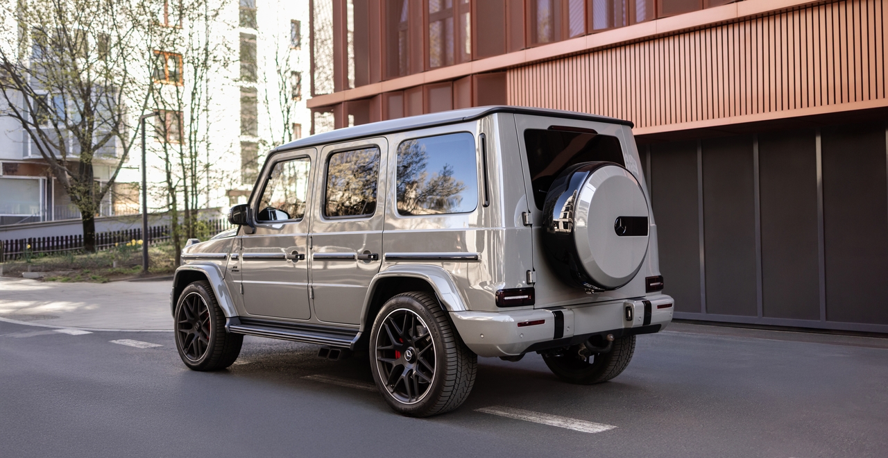 Задняя часть Mercedes-AMG G63 с характерным чехлом запаски и мощными колёсами на фоне городской архитектуры — стиль, узнаваемый с первого взгляда.