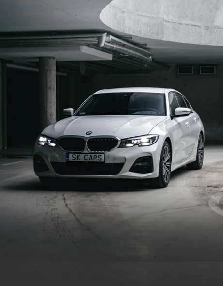 Передняя часть белого BMW 3 серии в стильной подземной парковке. Элегантность и мощь для вашего удовольствия от вождения.