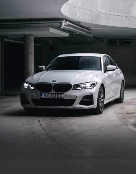 Передняя часть белого BMW 3 серии в стильной подземной парковке. Элегантность и мощь для вашего удовольствия от вождения.